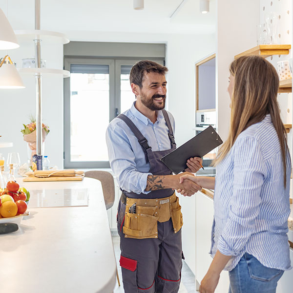 Young woman shaking hands to male plumber with clipboard in kitchen room
